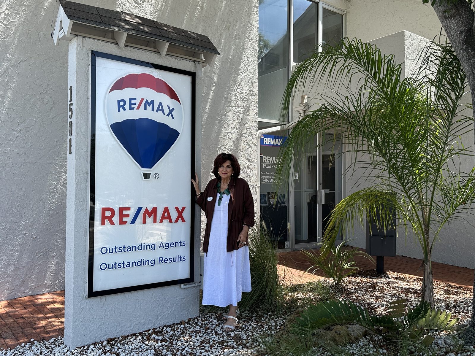Carole Samuels standing beside the RE/MAX balloon sign outside the RE/MAX Palm Realty office at 1501 Laurel Street in Sarasota, Florida